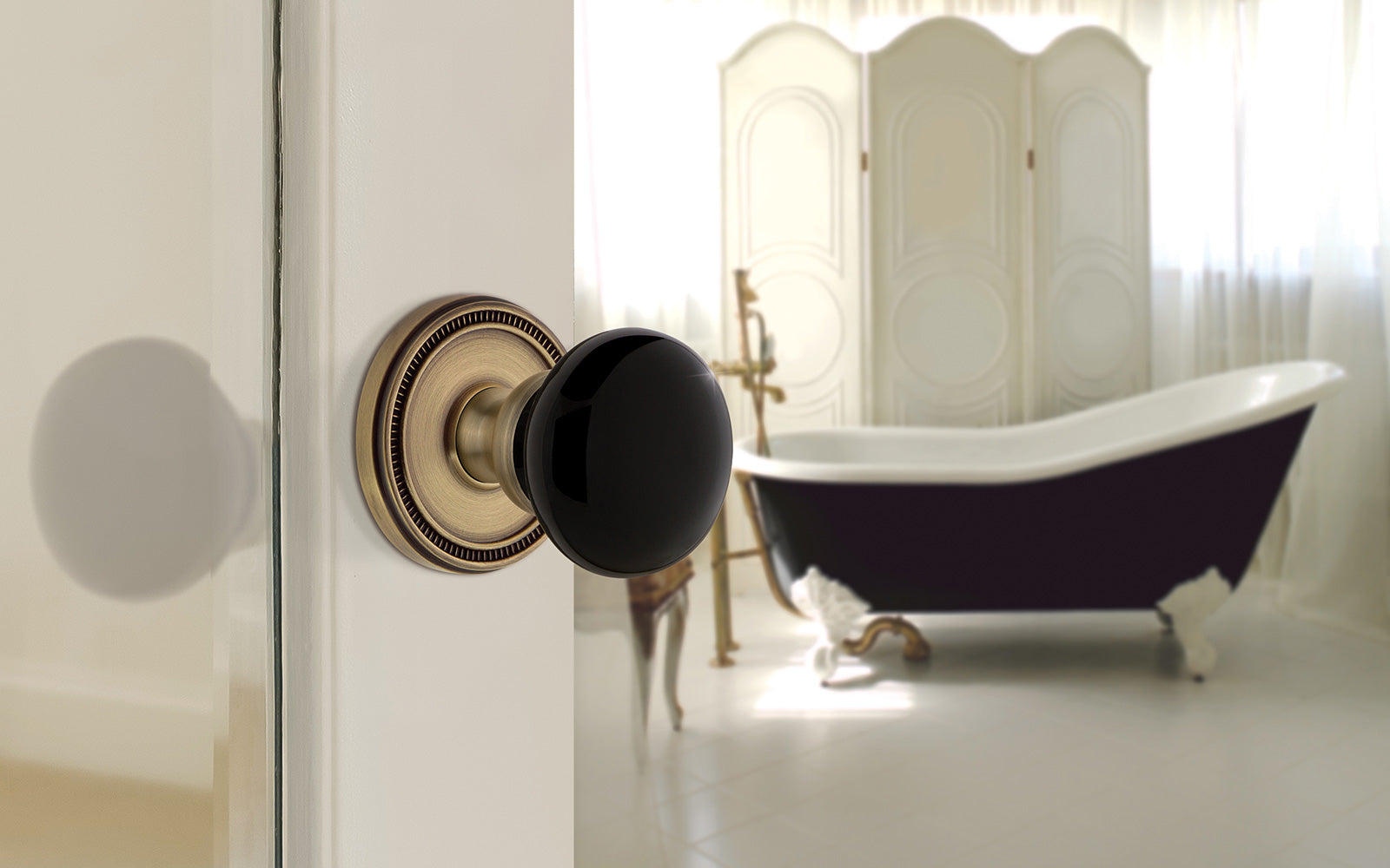 traditional home bathroom with black standing tub and vintage brass door hardware with black porcelain knob from grandeur hardware